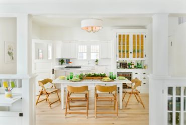 Bright white kitchen with wooden chairs around a table.