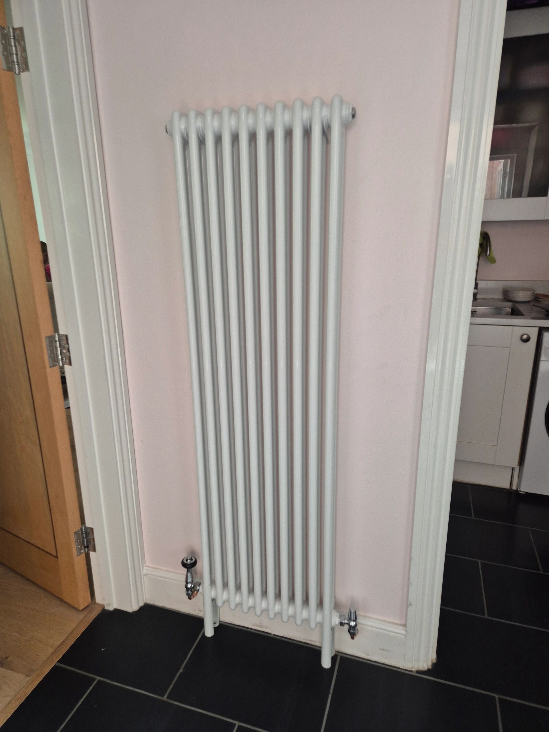 White vertical radiator against light pink wall.