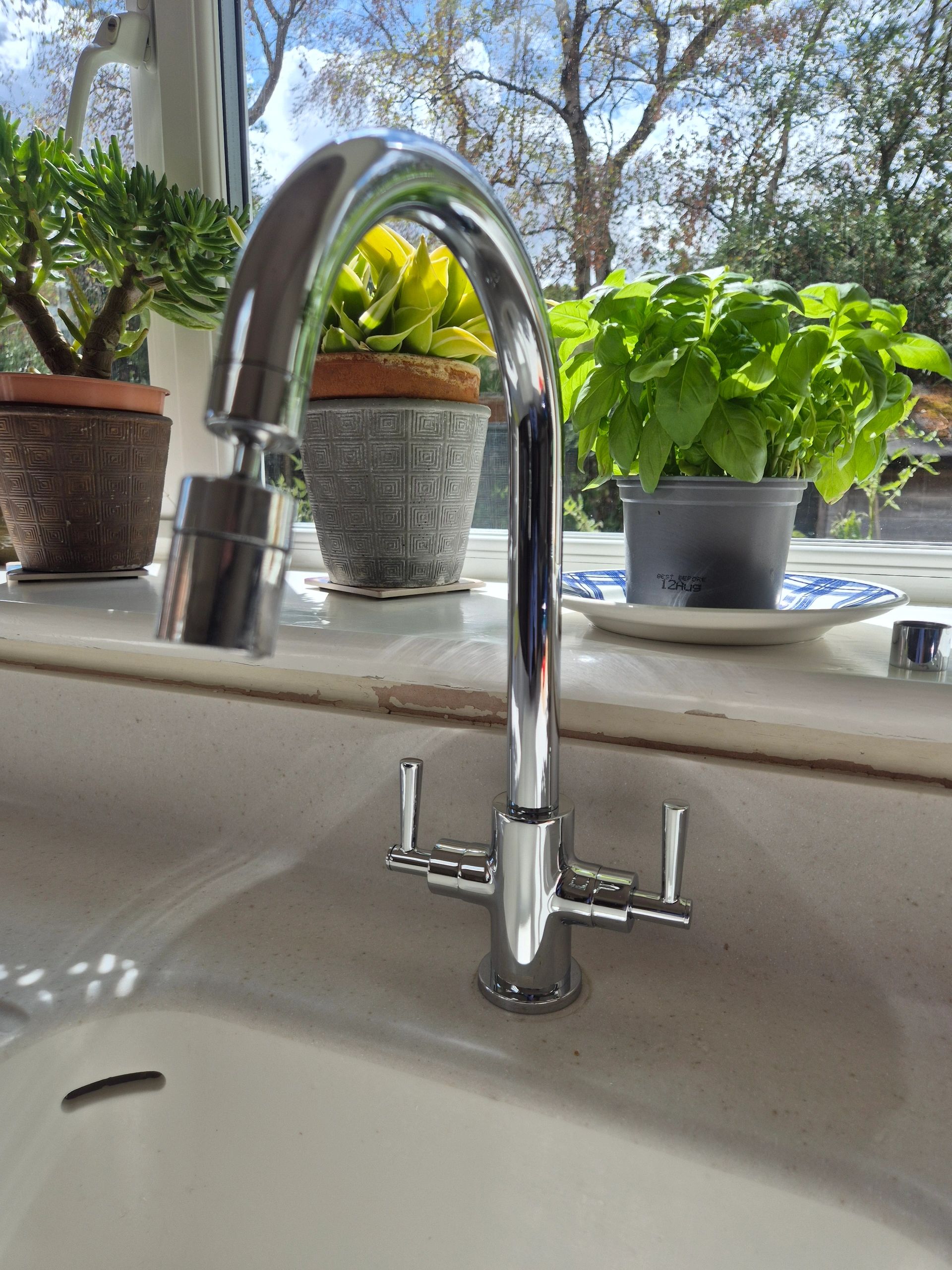Modern kitchen faucet with potted plants on the window sill.