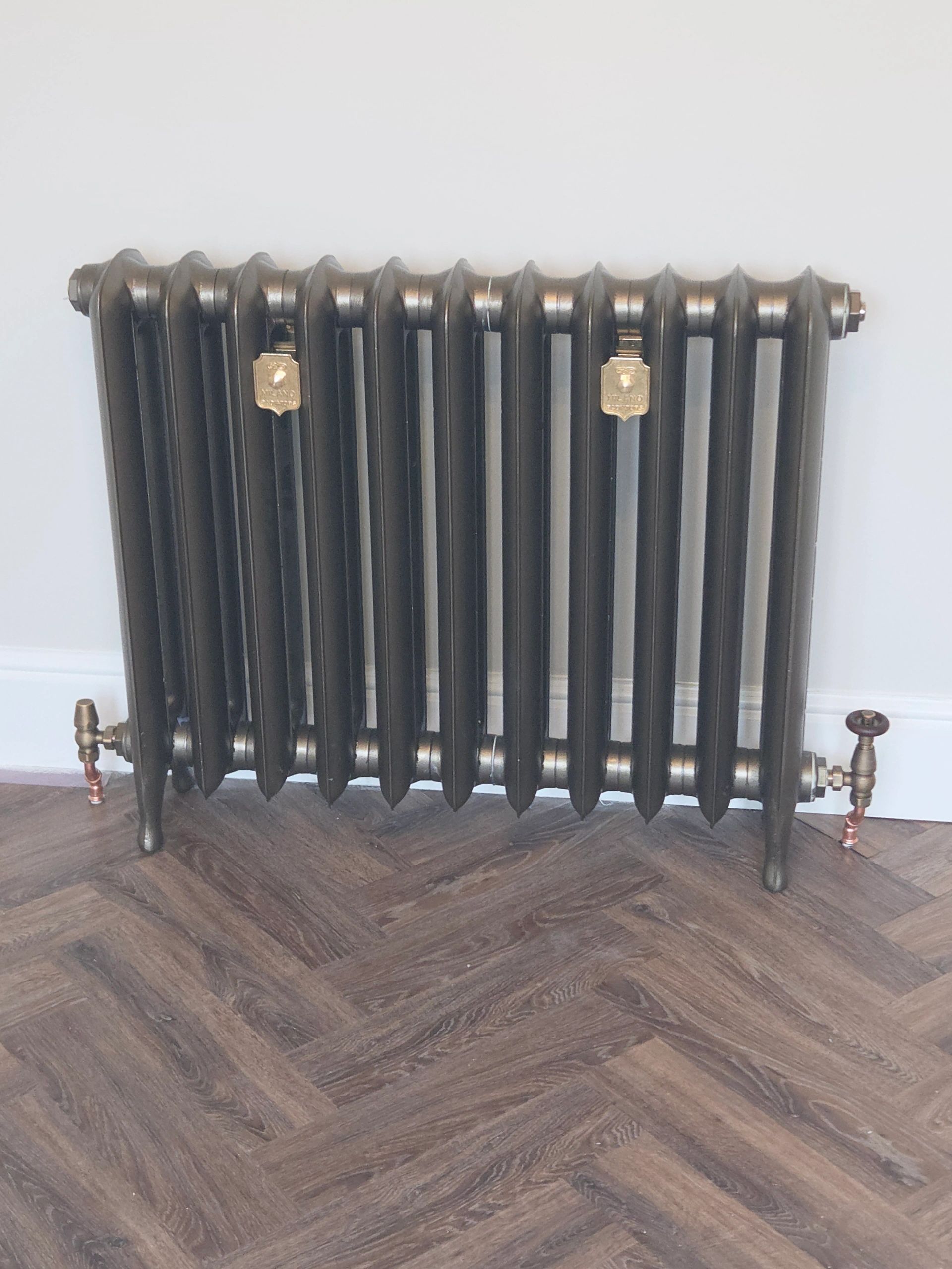 Black vintage radiator on wooden floor.