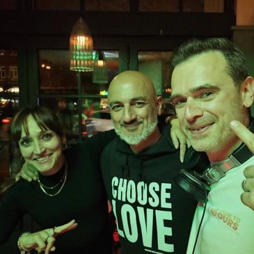 Three friends smiling together in a dimly lit room with warm green lighting.