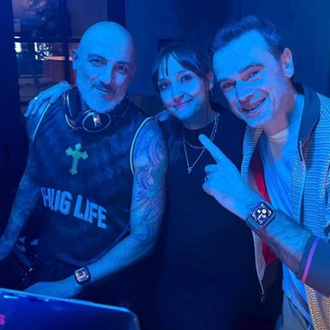Three people posing happily in blue lighting, one pointing at the DJ.