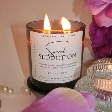 Lit scented candle named Secret Seduction with decorative flowers and pearls.