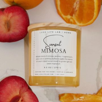 A Sunset Mimosa scented candle surrounded by fruit.