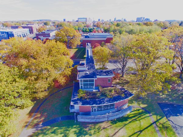 Aerial view of a modern building amidst autumn trees and urban skyline.