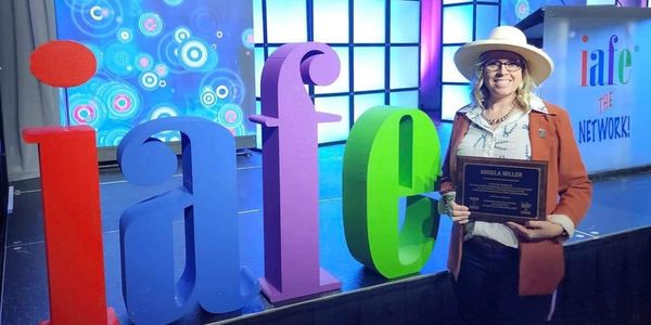 Woman holding award plaque next to colorful iafe letters.