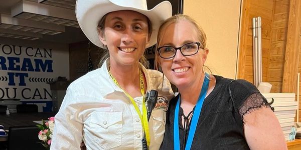 Two women smiling, one in a cowboy hat and the other with glasses.