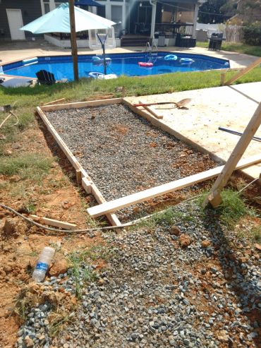 Construction site near a swimming pool with gravel and wooden frames.