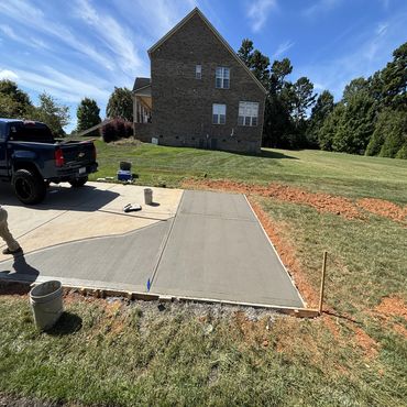 Newly poured concrete patio beside a house and truck.