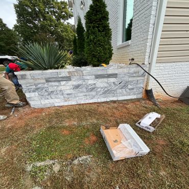 Man installing a stone planter by a house.