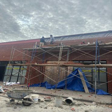 Two workers on scaffolding repairing brick wall under cloudy sky.