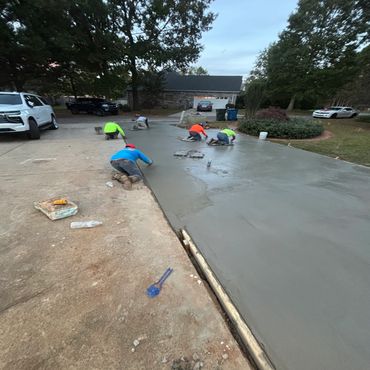 Workers smoothing fresh concrete on a driveway.