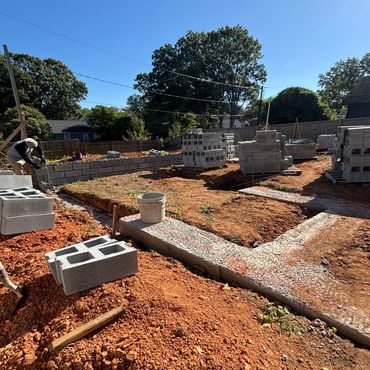 Worker building a cinder block wall on a sunny day.