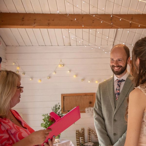 A groom smiles warmly during a wedding ceremony indoors.