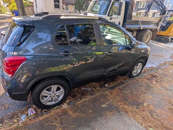 Black car with visible side damage parked on the street.