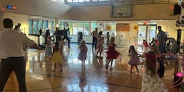 Children and adults dancing and playing in a gymnasium during a lively event.