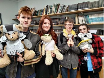Four young people holding stuffed animals dressed in costumes, smiling indoors.