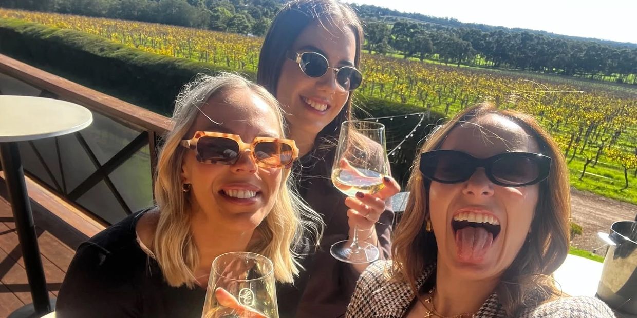 Three women wearing sunglasses enjoying drinks outdoors on a sunny day.