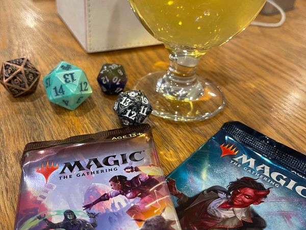 Magic: The Gathering booster packs with polyhedral dice and a drink on a wooden table.