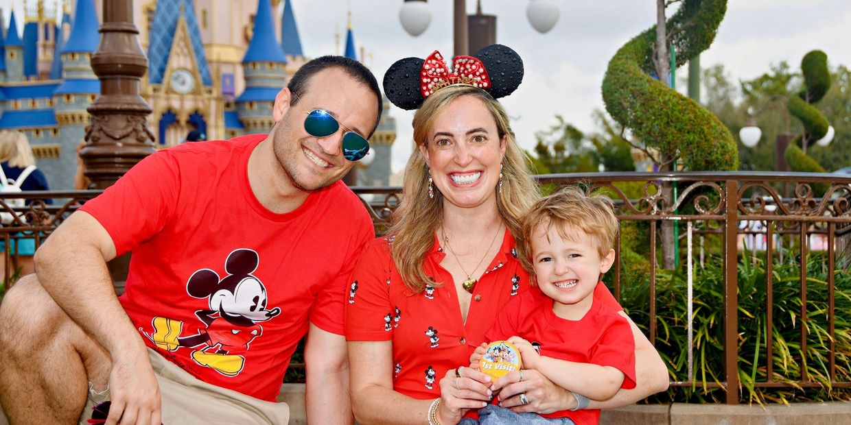 A happy family dressed in red Disney attire at a theme park.
