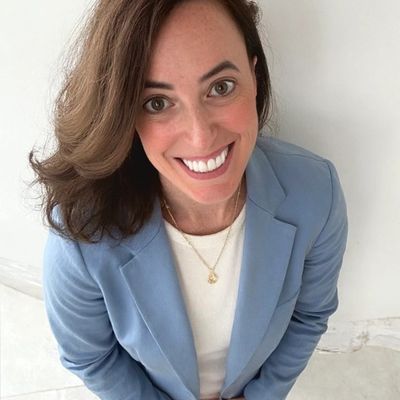 Smiling woman in a light blue blazer looking up at the camera.