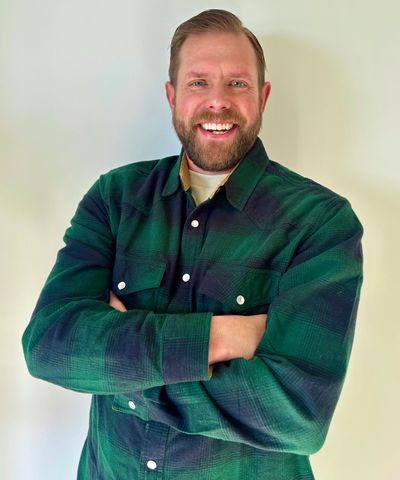 Smiling man in a green plaid shirt with arms crossed.