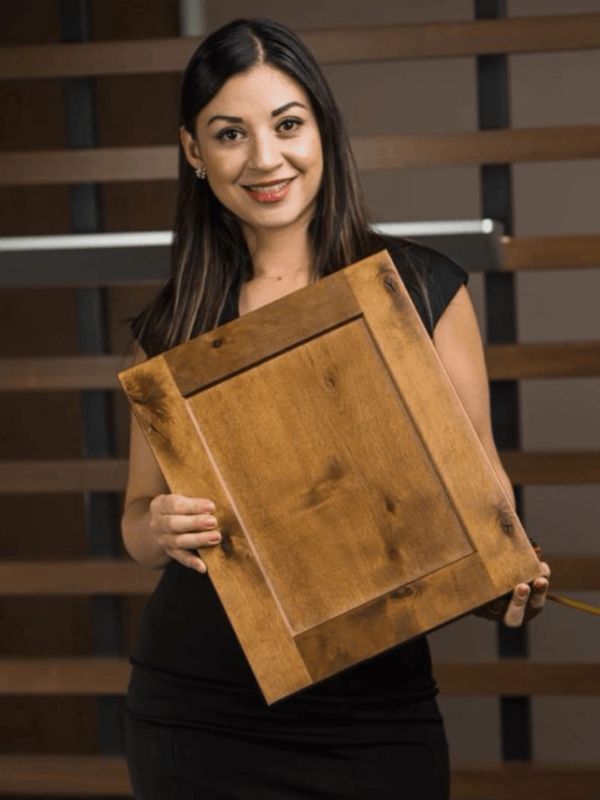 Smiling woman holding a wooden cabinet door panel.