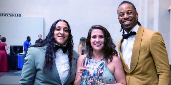 Three smiling people dressed formally, one holding an award.