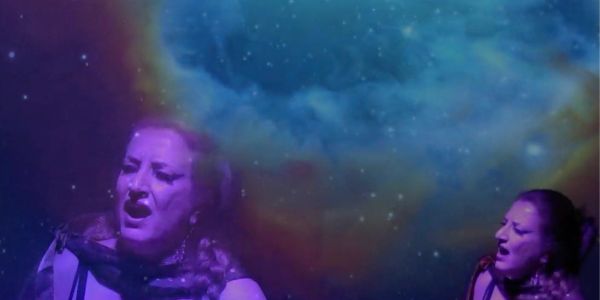 Two women singing with a cosmic background.