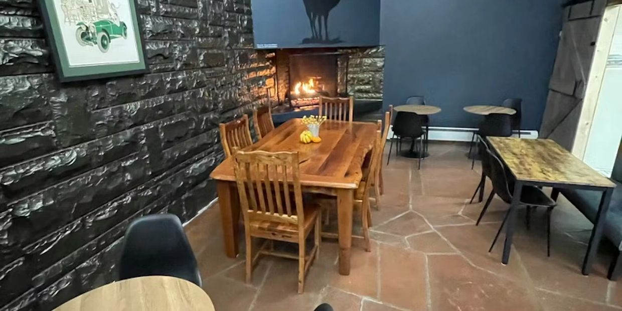 Cozy dining area with wooden tables and chairs near a lit fireplace.