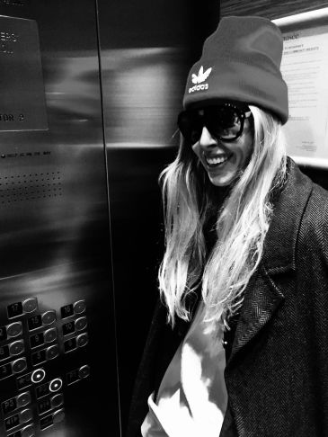 Smiling woman in sunglasses and beanie inside an elevator.