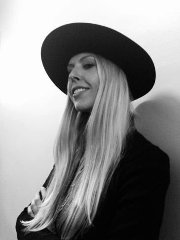 Woman with long blonde hair wearing a wide-brimmed hat and smiling.