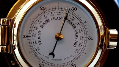 Close-up of a gold aneroid barometer measuring atmospheric pressure.