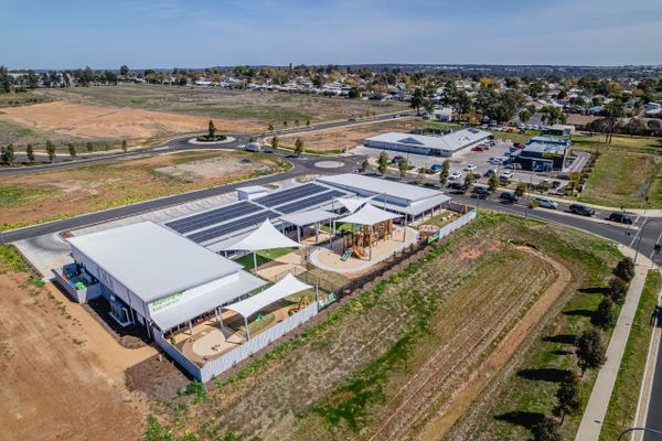 Aerial view of a modern childcare center with playgrounds and solar panels on the roof.