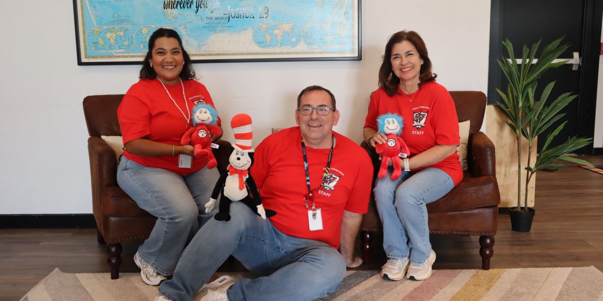 Three staff members wearing red shirts and holding Dr. Seuss stuffed toys.