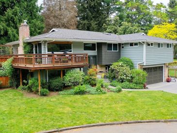 A two-story suburban house with a wooden deck and lush garden.