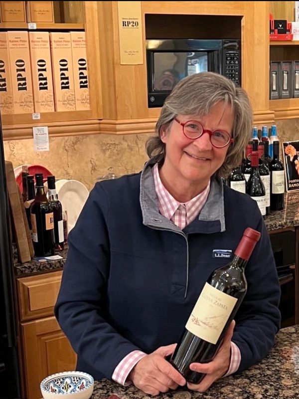 Smiling woman in red glasses holding a wine bottle in a kitchen.