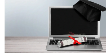 Open laptop with a diploma on the keyboard and a graduation cap hanging on the top of the screen. 