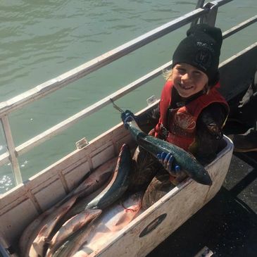 Smiling child in wetsuit holding a fish on a boat with several fish in a cooler.