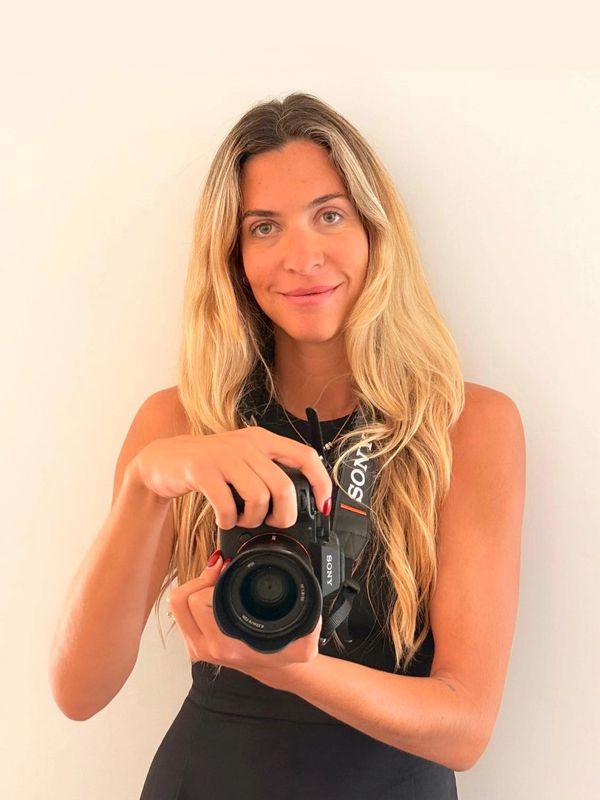 A smiling woman with long blonde hair holding a Sony camera.
