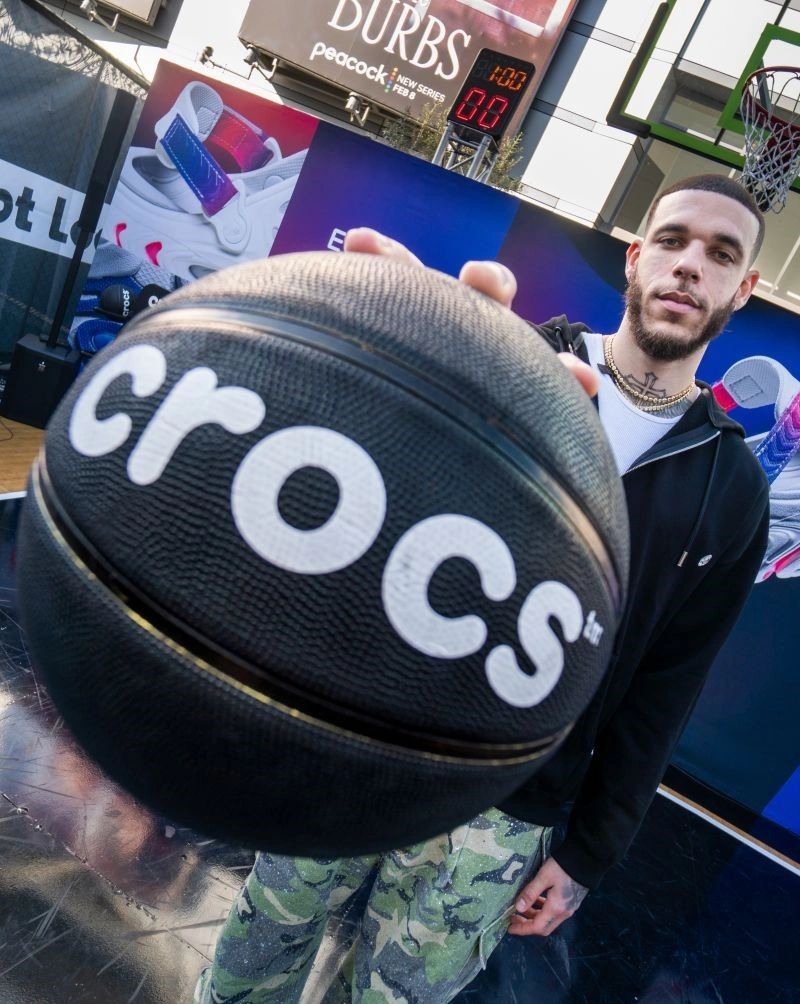 Man holding a basketball with Crocs logo, standing on a basketball court.