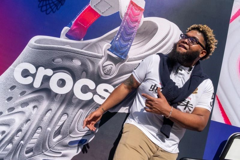 Man posing in front of a giant Crocs shoe advertisement.