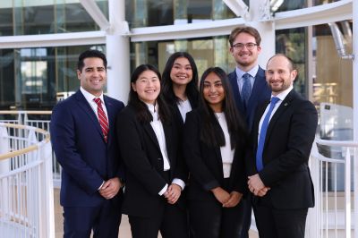 Group of six professionals posing outdoors in business attire.