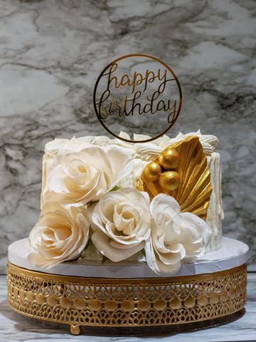 Decorative gold and white birthday cake with white flowers, gold accents and a happy birthday sign
