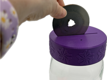 Hand placing a black washer into a purple-lidded jar.
