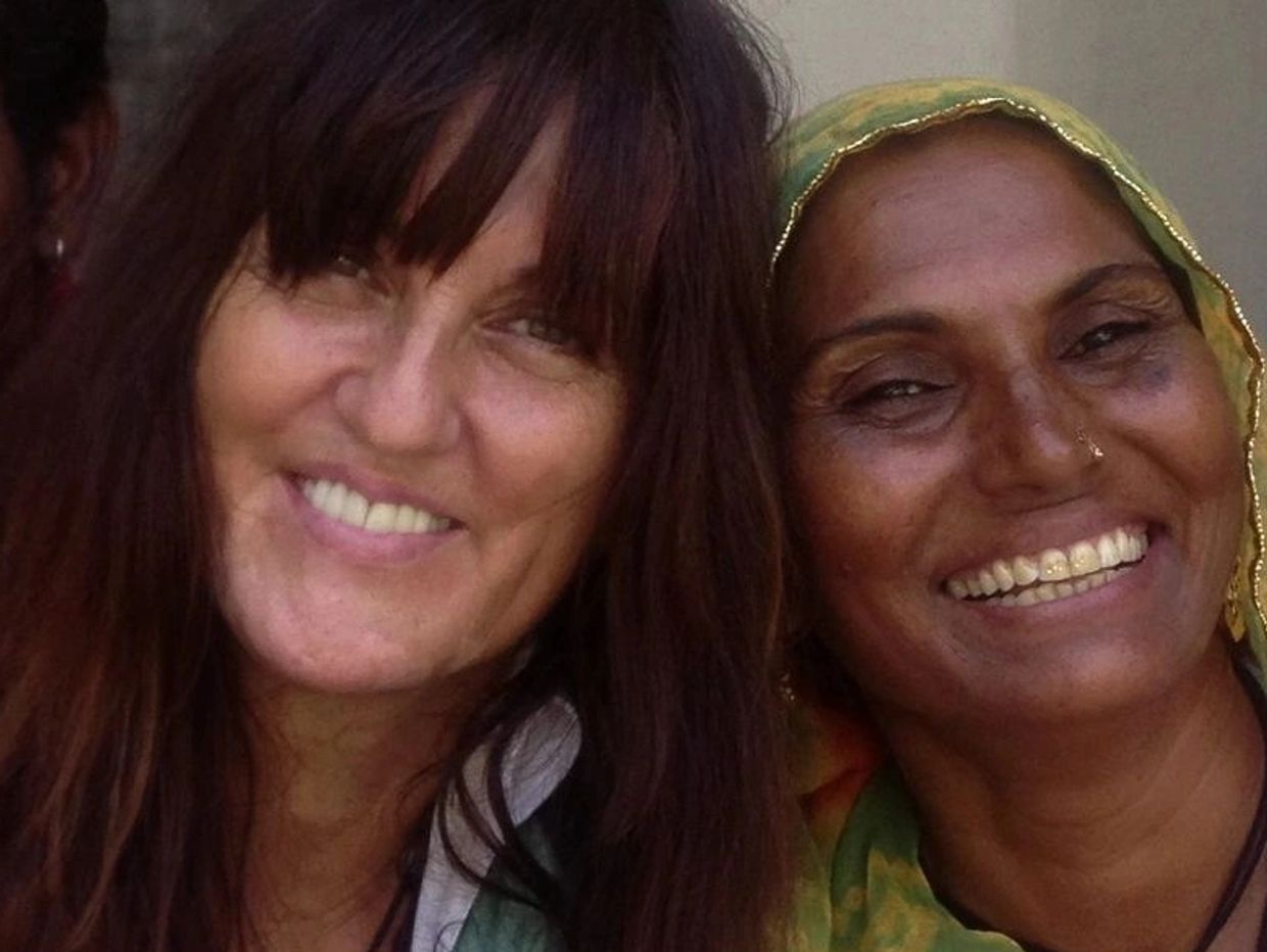 Close-up of two smiling women wearing colorful clothing and necklaces.
