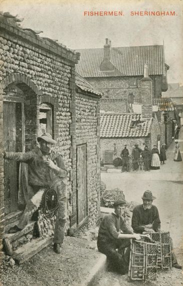 Fishermen in Sheringham resting by stone buildings with fishing gear.