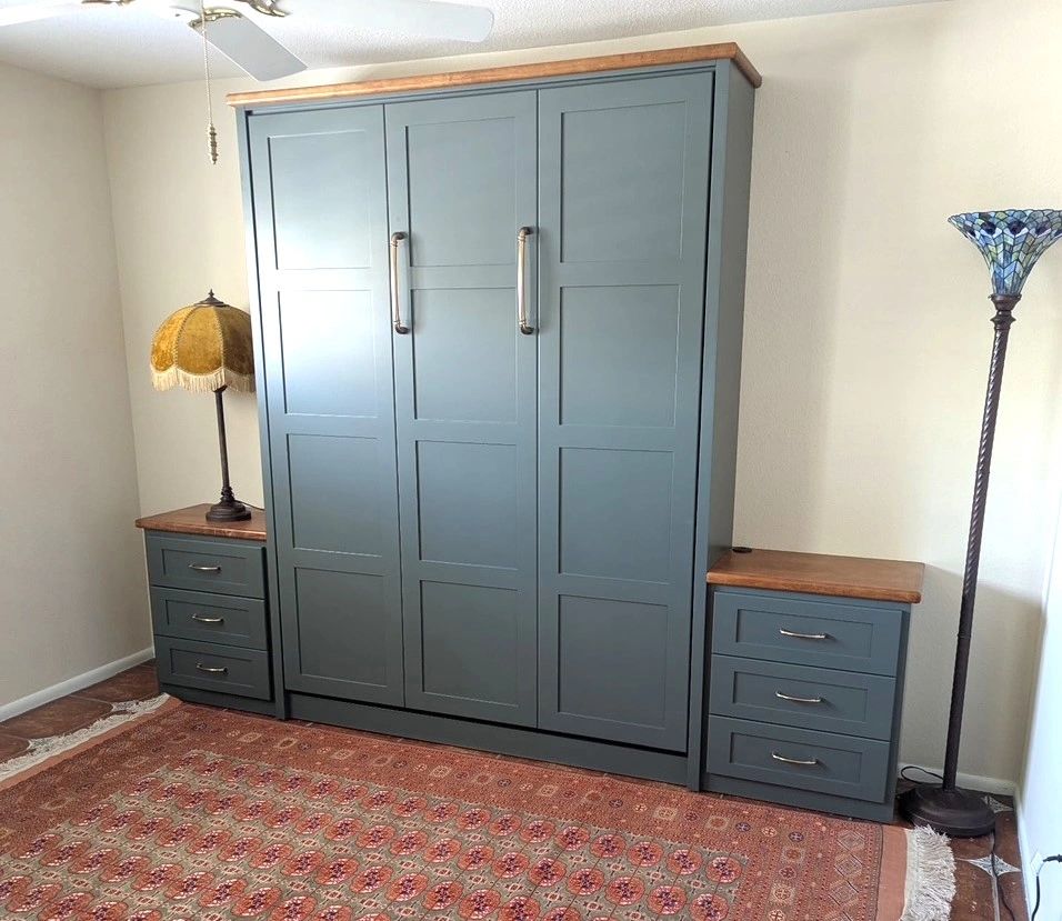 Blue wardrobe with wooden tops flanked by two drawer units, vintage lamps on each side.