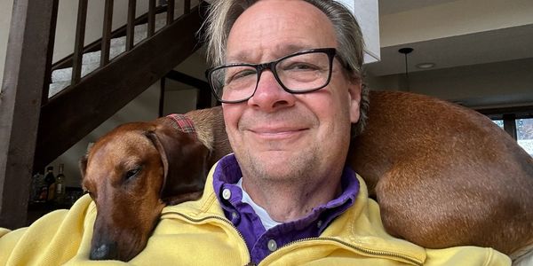 Man wearing glasses with a brown dog resting on his shoulder.