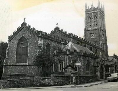 Historic stone church with a tall clock tower on a street corner.